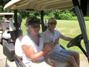 Two people in a golf cart driving on the course.