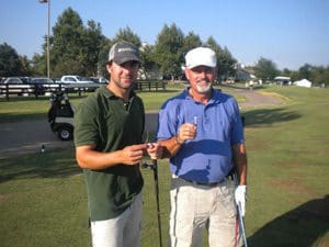 Two men standing on a golf course holding onto their clubs.
