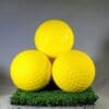 Three yellow golf balls on a green mat.