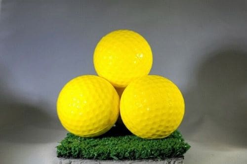 Three yellow golf balls on a green mat.